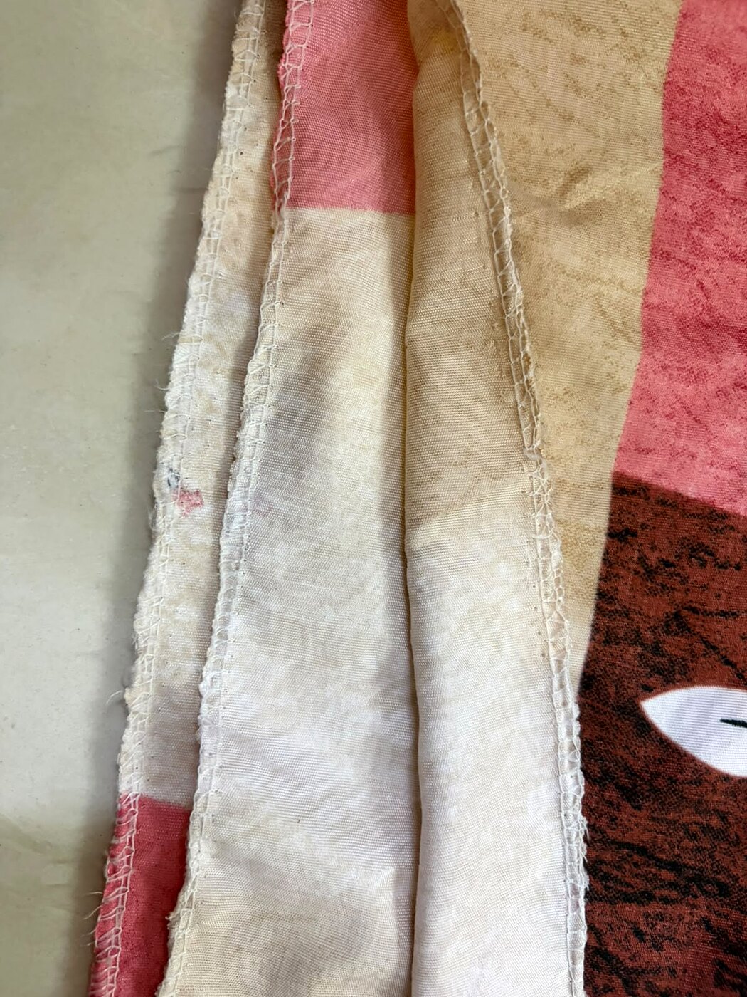 Close-up of budget bedsheet edge showing thin frayed overlock stitch with minimal reinforcement